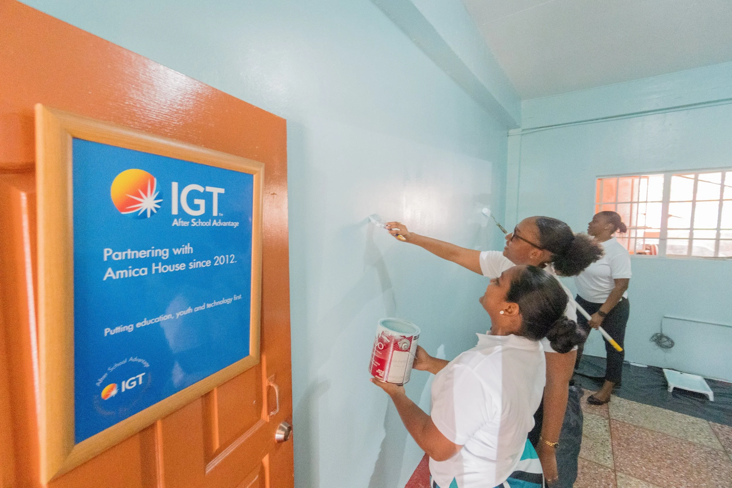In May 2024, IGT staff Tanya Singh, IGT Global People Services Representative (front), Chelsea Alleyne, IGT Administrative Assistant (centre), and Akilah Howard, IGT Call Center Associate, volunteered to paint and refresh the computer room at Amica House.
